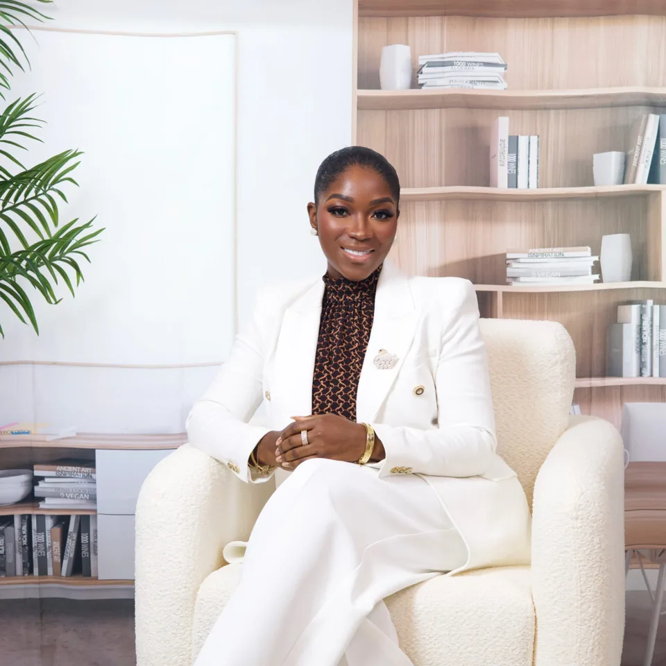 Evon Anthony seated in a cream armchair wearing a white blazer, in front of a bookshelf
